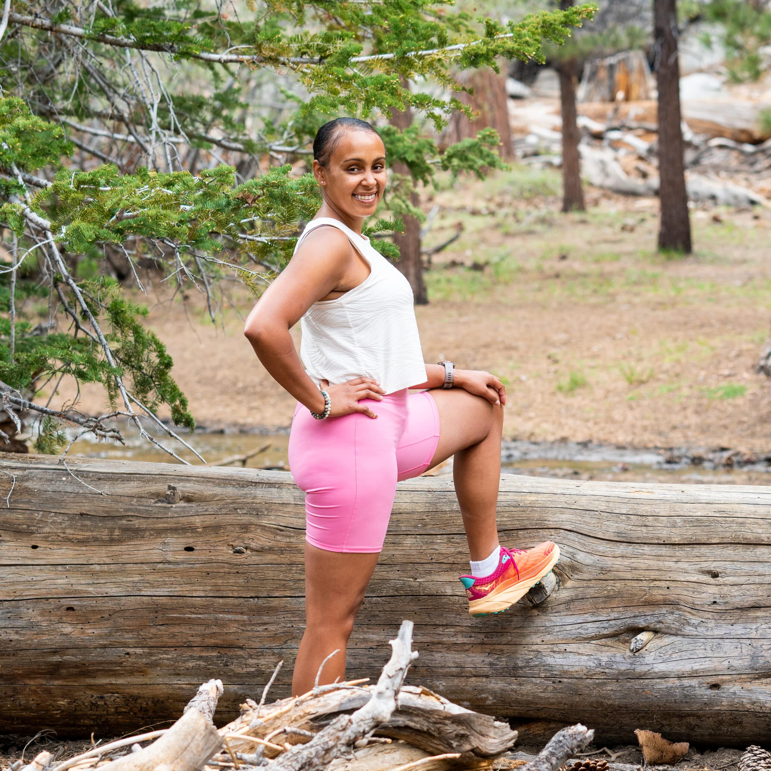 A woman is posing About Us in the woods on a log.