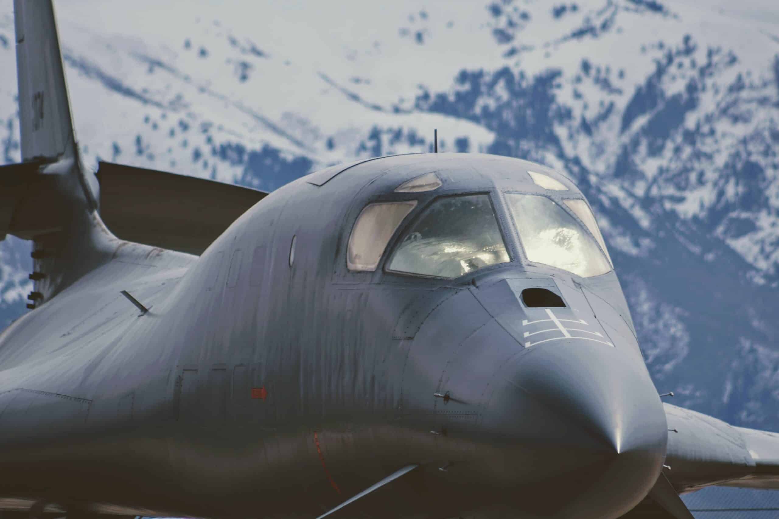 A black military jet parked in front of snowy mountains.