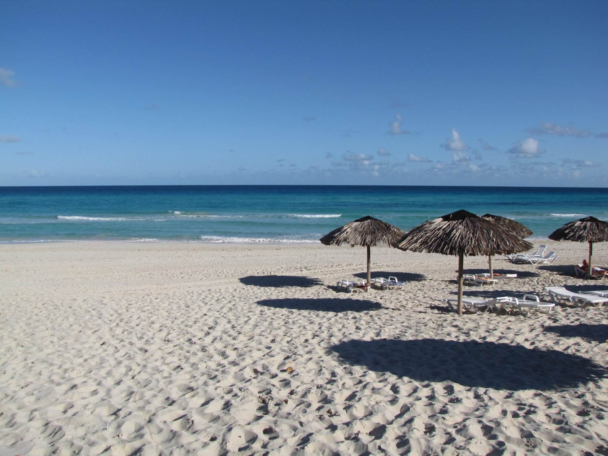 A beach with lounge chairs and umbrellas on the sand.