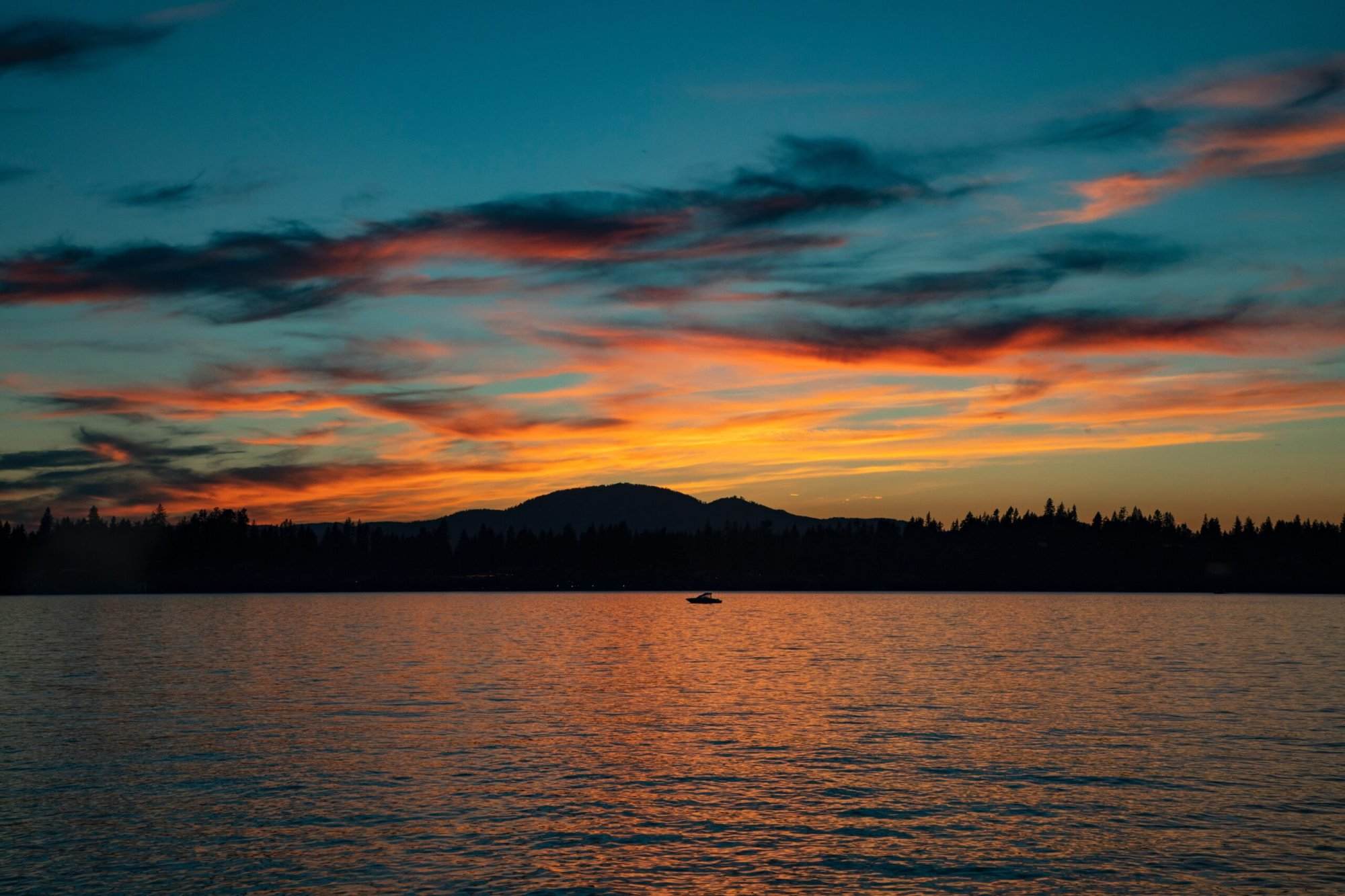 A sunset over a lake with a mountain in the background.