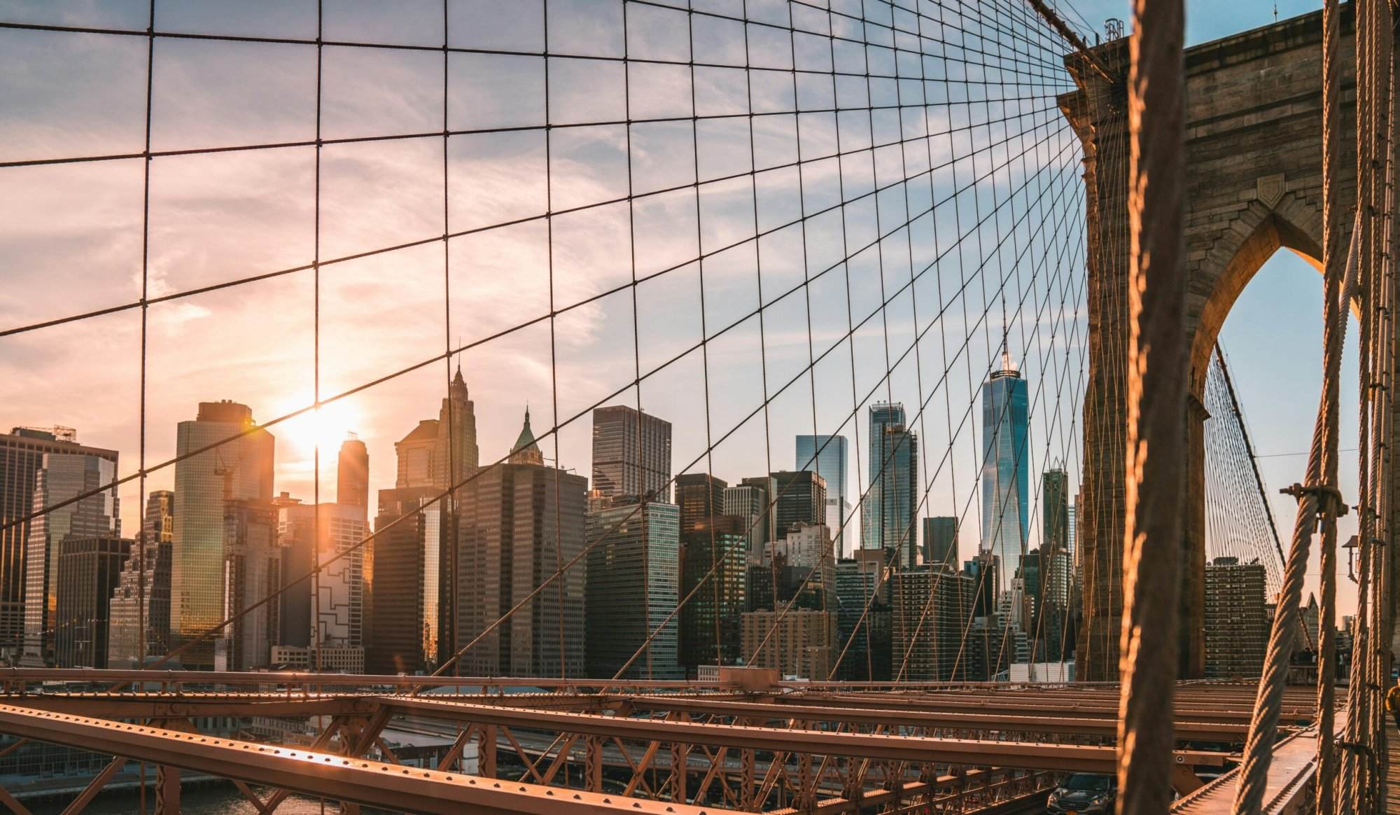 Golden hour over Manhattan, viewed through the cables of the Brooklyn Bridge, becomes a serene backdrop to the NYRR marathon runners.