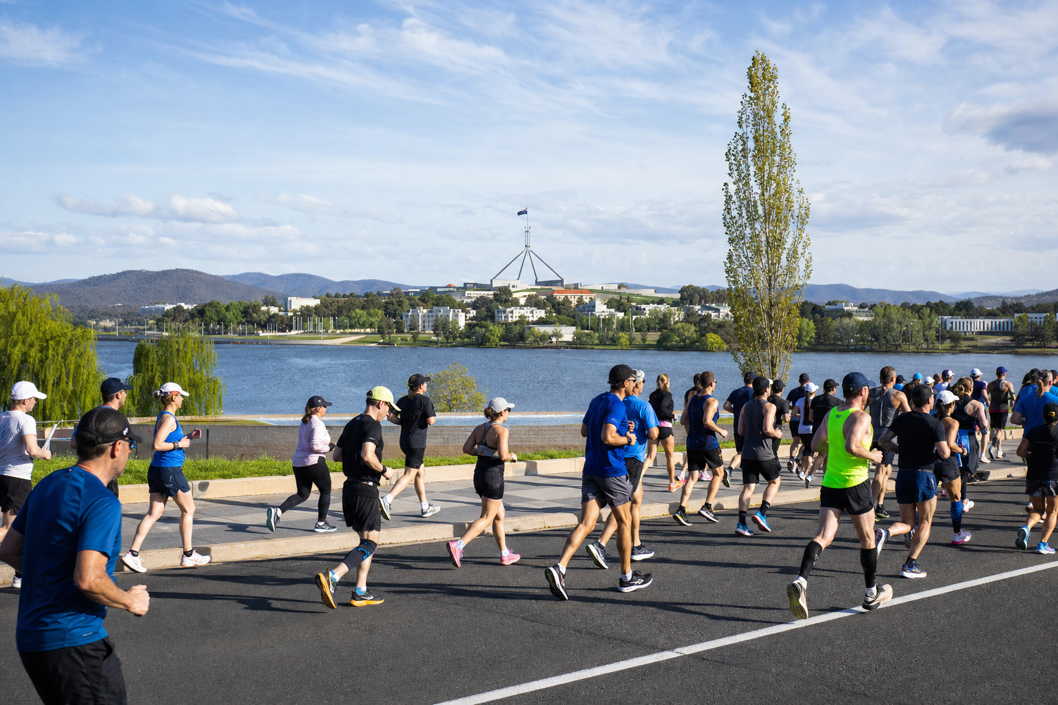Runners participate in a road race beside a lake, with Parliament House visible on the distant hill in Canberra.